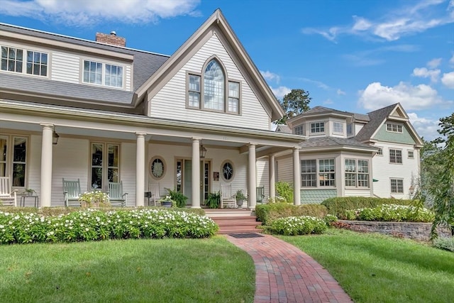 view of front facade with a front lawn, a chimney, a porch, and a shingled roof