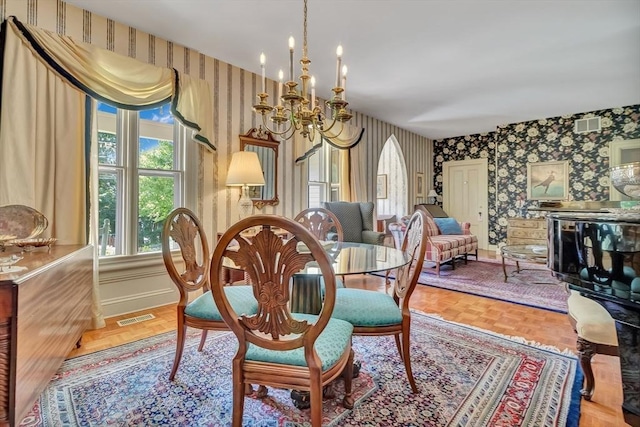 dining space featuring a chandelier, visible vents, baseboards, and wallpapered walls