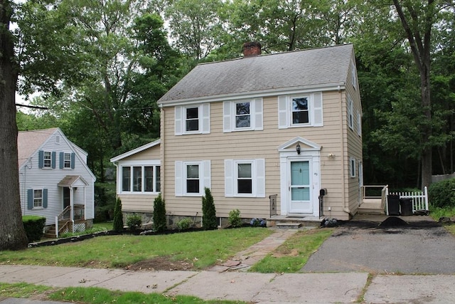 49 Newcomb Rd, Stoneham, MA 02180 - colonial home featuring a chimney, a front yard, view of scattered trees, and roof with shingles