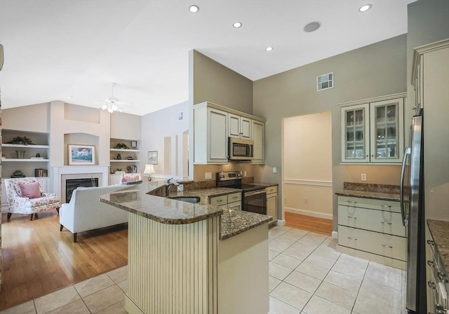 kitchen featuring light tile patterned flooring, sink, appliances with stainless steel finishes, kitchen peninsula, and dark stone counters