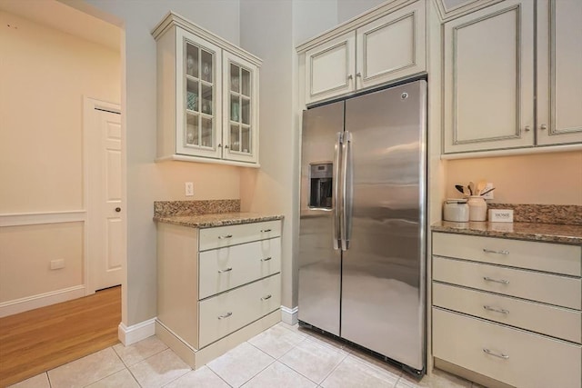 kitchen featuring cream cabinets, stone countertops, stainless steel fridge with ice dispenser, and light tile patterned floors