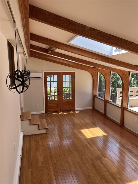 interior space featuring a wall mounted air conditioner, french doors, vaulted ceiling with skylight, a baseboard heating unit, and dark hardwood / wood-style floors