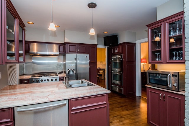 kitchen featuring dark wood-type flooring, sink, wall chimney exhaust hood, appliances with stainless steel finishes, and decorative light fixtures