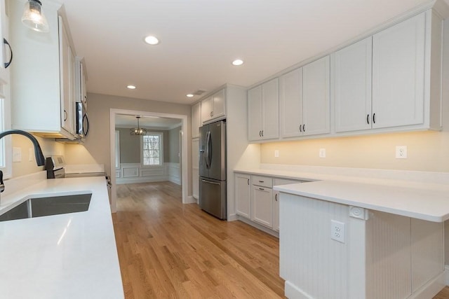 kitchen featuring light countertops, a sink, light wood finished floors, and stainless steel appliances