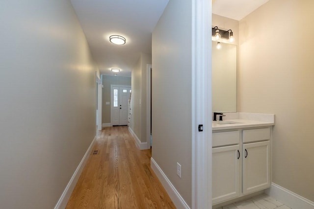 hallway with baseboards, a sink, light wood finished floors, and visible vents
