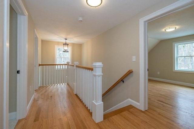 hallway featuring baseboards, an upstairs landing, and light wood-style flooring