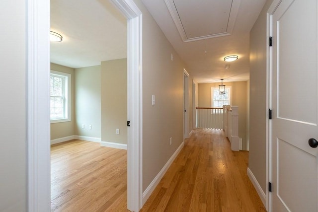 hall featuring baseboards, attic access, light wood-style flooring, and an upstairs landing