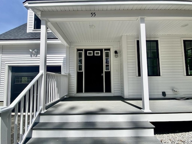 view of exterior entry featuring covered porch and roof with shingles