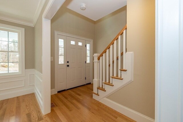 entryway with visible vents, crown molding, wainscoting, stairway, and light wood finished floors