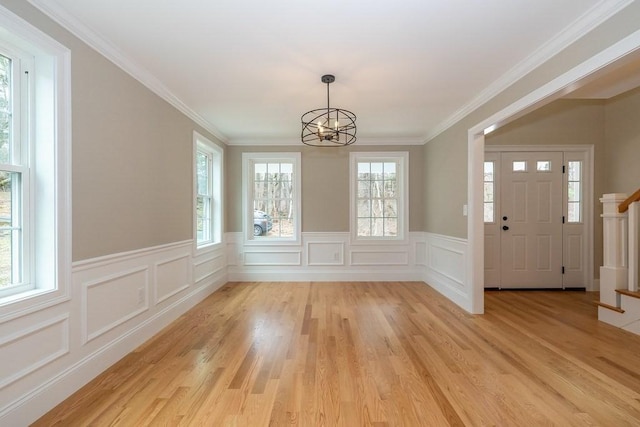 unfurnished dining area featuring a decorative wall, wainscoting, light wood-style flooring, and a chandelier