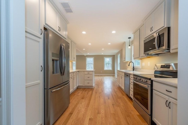 kitchen featuring visible vents, a peninsula, light countertops, light wood finished floors, and appliances with stainless steel finishes