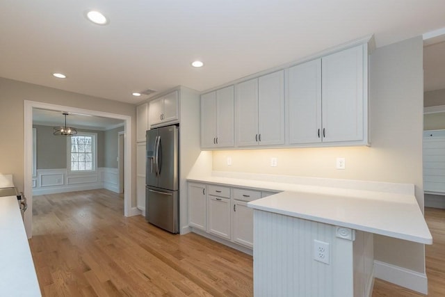 kitchen featuring light countertops, a peninsula, stainless steel fridge, and light wood-style floors