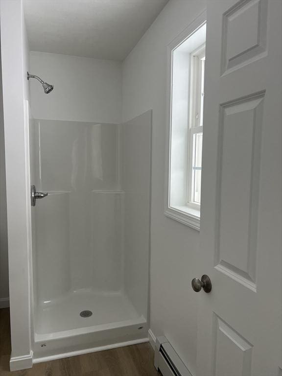 bathroom with hardwood / wood-style flooring, a shower, and a baseboard heating unit