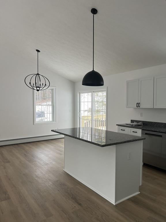 kitchen with dark wood-type flooring, hanging light fixtures, dark stone countertops, stainless steel dishwasher, and a kitchen island