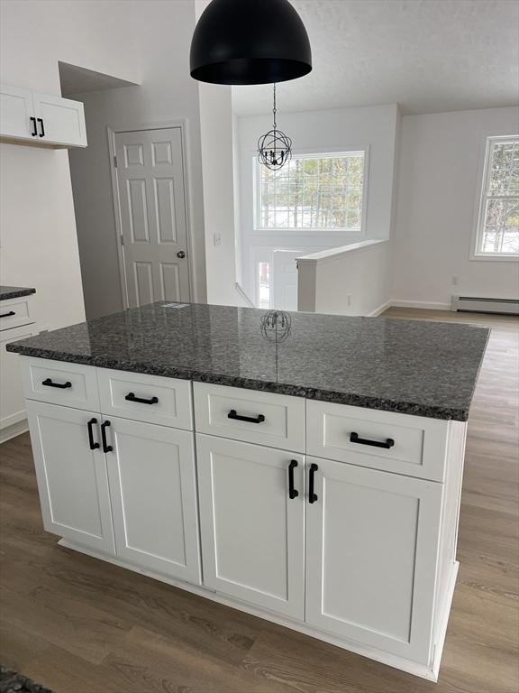 kitchen with white cabinetry, wood-type flooring, a kitchen island, and dark stone countertops