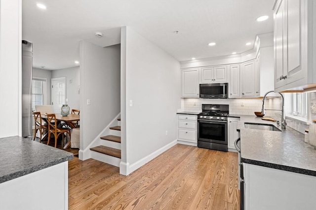 kitchen with appliances with stainless steel finishes, a sink, dark countertops, light wood-style floors, and white cabinets