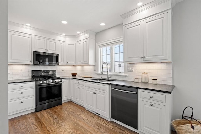 kitchen with appliances with stainless steel finishes, a sink, dark countertops, light wood-type flooring, and recessed lighting