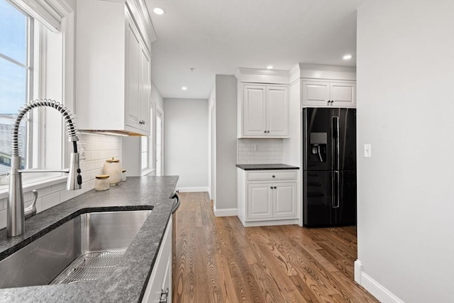 kitchen featuring black fridge with ice dispenser, a sink, baseboards, tasteful backsplash, and light wood finished floors