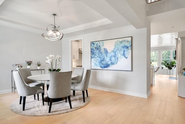 dining area with a chandelier, ornamental molding, a raised ceiling, and light hardwood / wood-style flooring