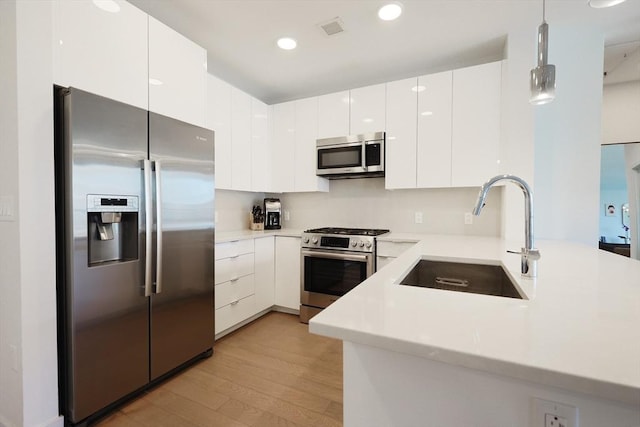 kitchen featuring appliances with stainless steel finishes, sink, light wood-type flooring, white cabinets, and hanging light fixtures