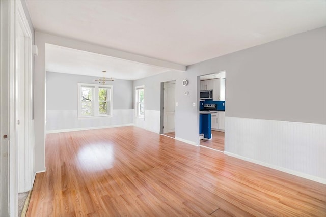 12 Cross St, Pepperell, MA 01463 - empty room featuring a chandelier, light wood-style floors, a wainscoted wall, and beam ceiling