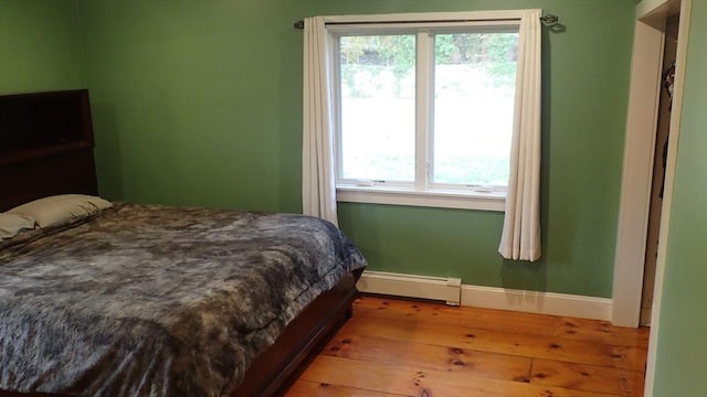 bedroom with wood-type flooring, multiple windows, and baseboard heating