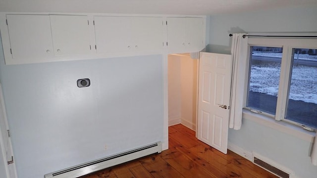 laundry room with a baseboard heating unit, dark wood-type flooring, and cabinets