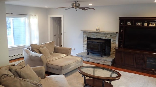 living room featuring ceiling fan, a baseboard heating unit, a wood stove, and wood-type flooring