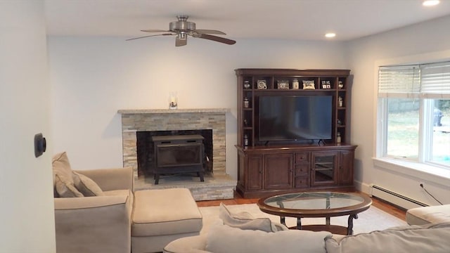 living room with baseboard heating, ceiling fan, light hardwood / wood-style flooring, and a wood stove