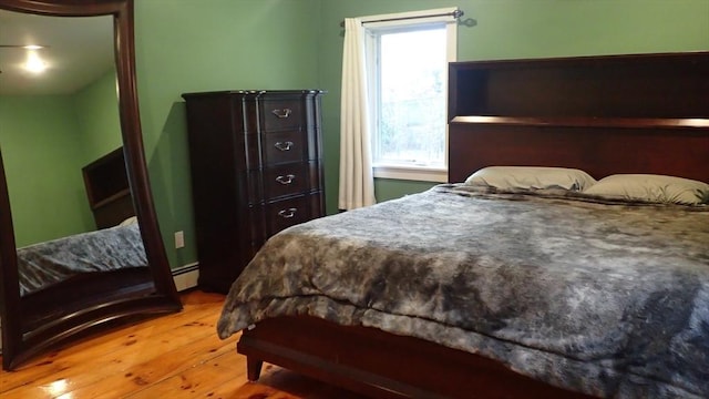 bedroom with a baseboard heating unit and light hardwood / wood-style flooring