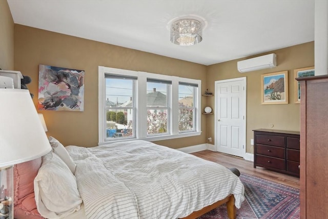 bedroom featuring an AC wall unit, wood finished floors, and baseboards