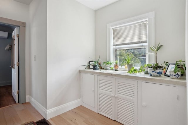 bar with an AC wall unit, light wood-style flooring, and baseboards