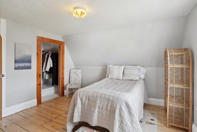 bedroom featuring baseboards, light wood-type flooring, a heating unit, and vaulted ceiling