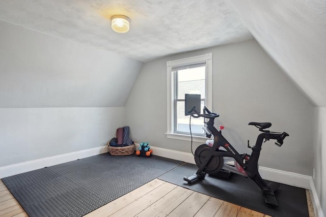 exercise room with baseboards, a textured ceiling, lofted ceiling, and wood-type flooring