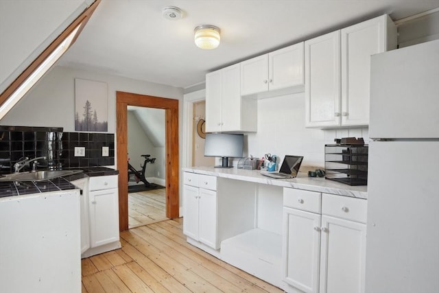 kitchen featuring a sink, tile counters, tasteful backsplash, white cabinetry, and freestanding refrigerator