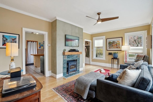 living area featuring light wood-style flooring, a ceiling fan, ornamental molding, and baseboards
