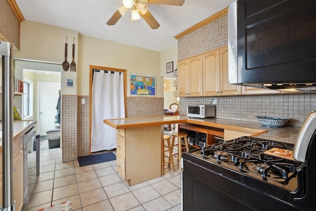 kitchen featuring light tile patterned flooring, ceiling fan, a breakfast bar area, light brown cabinetry, and a peninsula