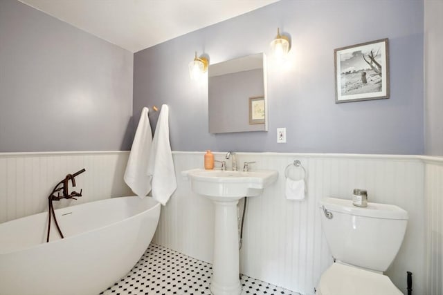 bathroom with toilet, a wainscoted wall, and a freestanding tub