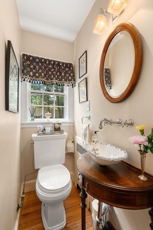 half bathroom featuring baseboards, wood finished floors, toilet, and a sink