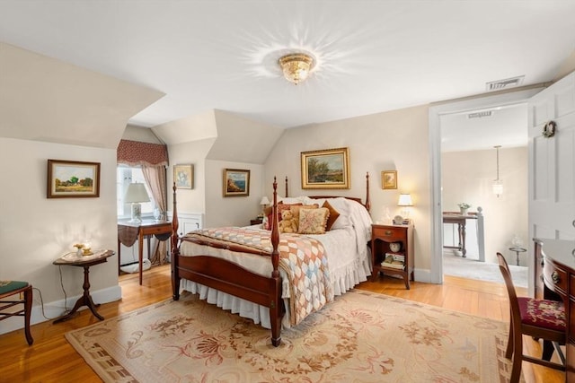 bedroom with visible vents, light wood finished floors, and vaulted ceiling