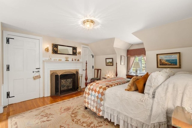 bedroom with lofted ceiling, wood finished floors, and a fireplace