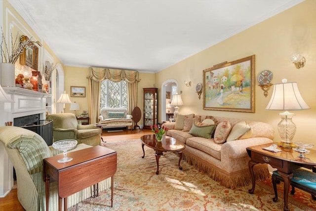 living room featuring ornamental molding, arched walkways, wood finished floors, and a fireplace
