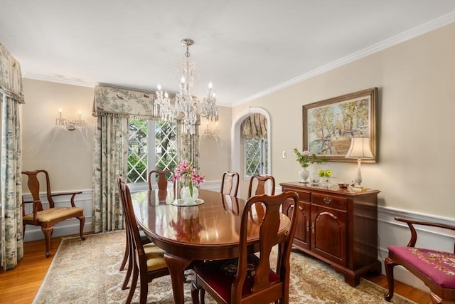 dining area with crown molding, a wainscoted wall, a notable chandelier, and light wood-style flooring