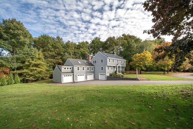 rear view of property with aphalt driveway, a yard, and a chimney
