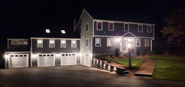 colonial-style house with aphalt driveway, an attached garage, and a yard