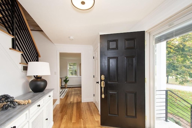 foyer with baseboard heating, ornamental molding, stairs, and light wood finished floors