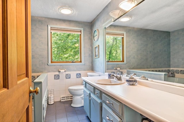 full bathroom featuring a textured ceiling, toilet, tile patterned flooring, vanity, and wainscoting