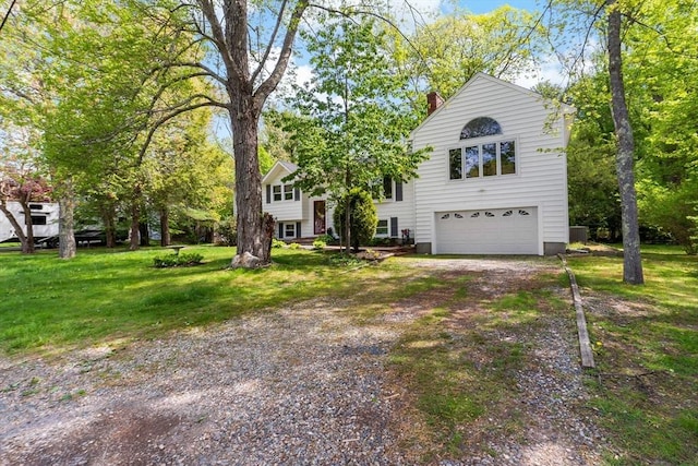 bi-level home with an attached garage, driveway, a chimney, and a front lawn
