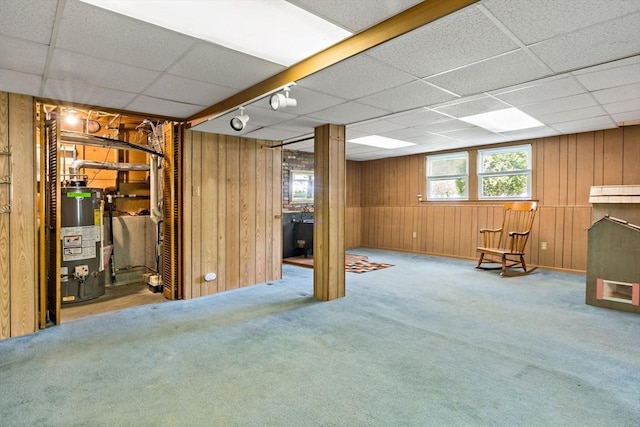 basement featuring gas water heater, a paneled ceiling, wooden walls, and carpet flooring