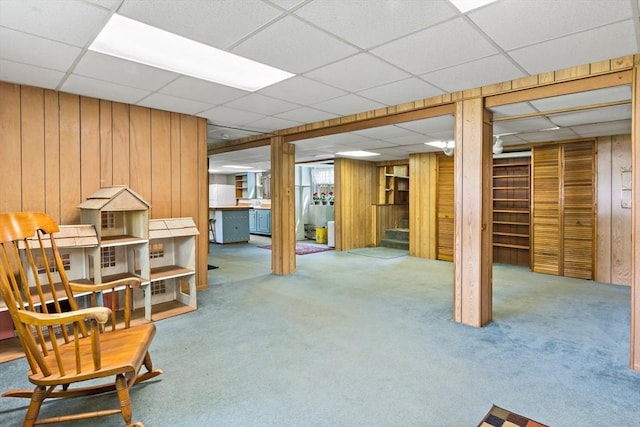 finished below grade area with a drop ceiling, carpet, wood walls, and stairs